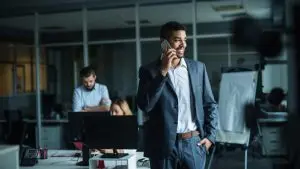 Un homme en costume utilise un téléphone portable dans un environnement de bureau, illustrant l'importance des communications téléphoniques en entreprise.