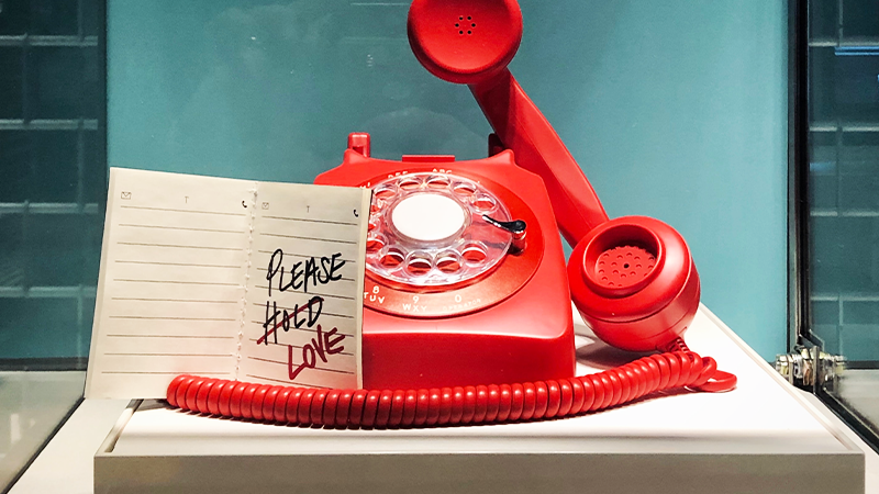 Téléphone rétro rouge avec un message écrit "Please hold love" posé à côté