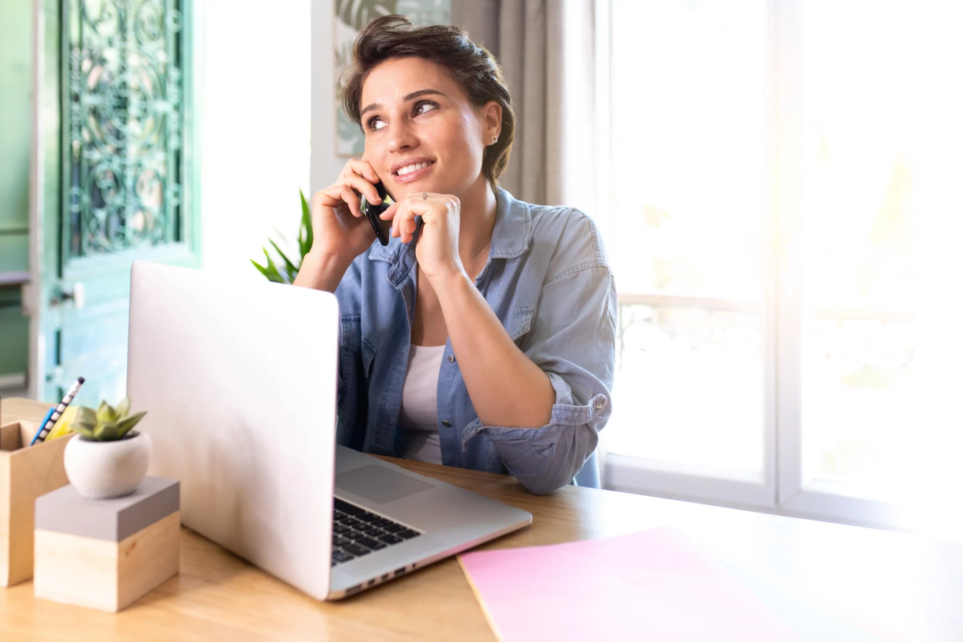 Femme d'affaires discutant au téléphone tout en travaillant sur son ordinateur portable dans un bureau moderne.