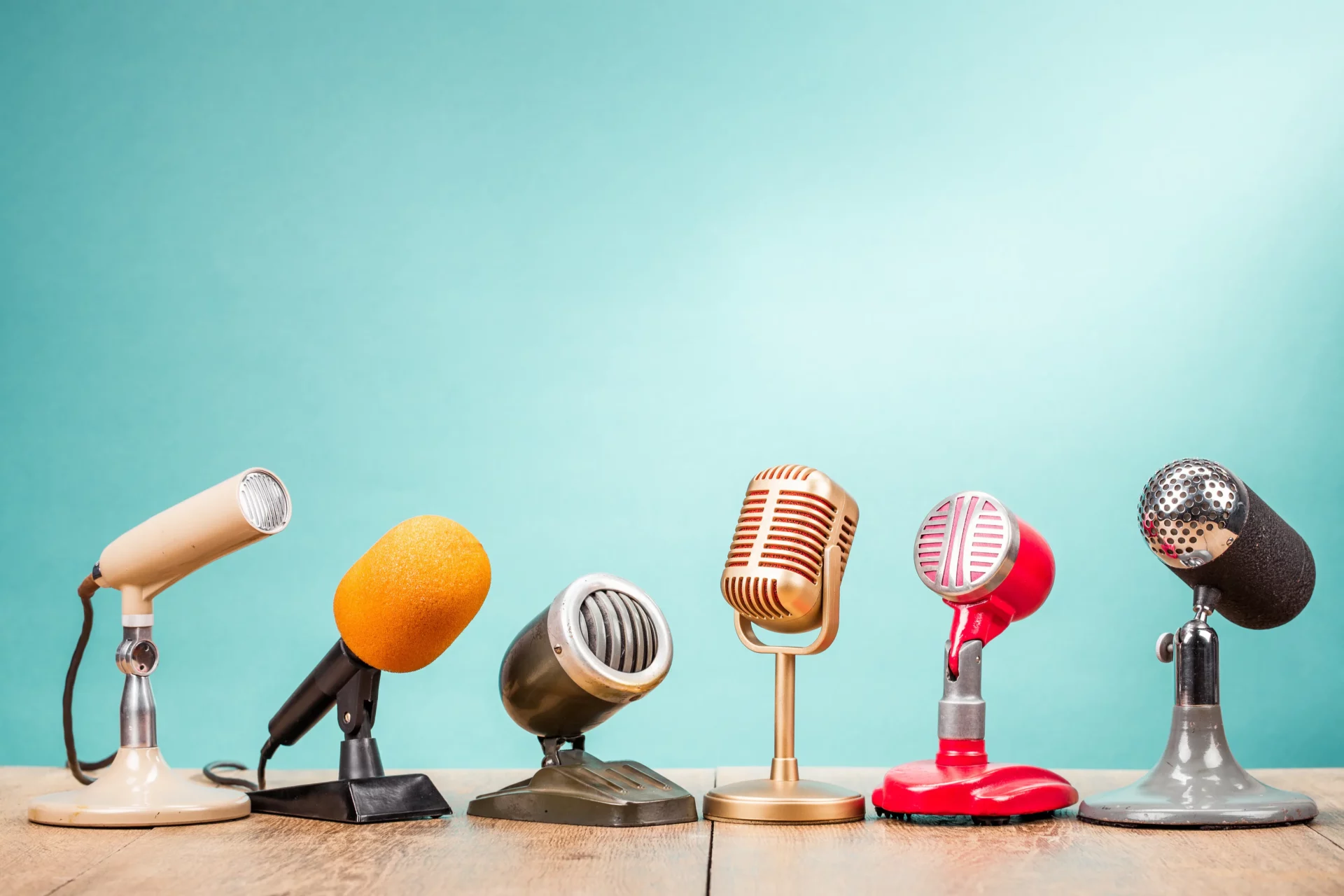 Plusieurs microphones vintage alignés sur une table en bois avec un fond bleu