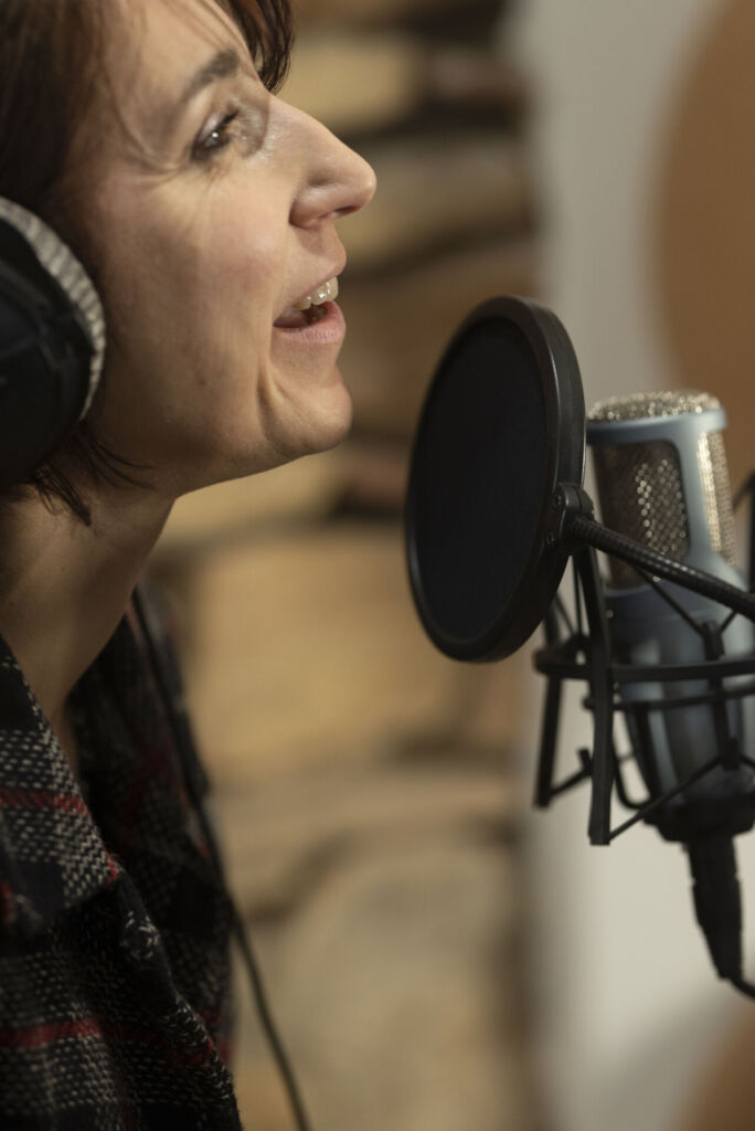 Femme enregistrant une voix-off dans un studio professionnel avec un microphone et un casque.