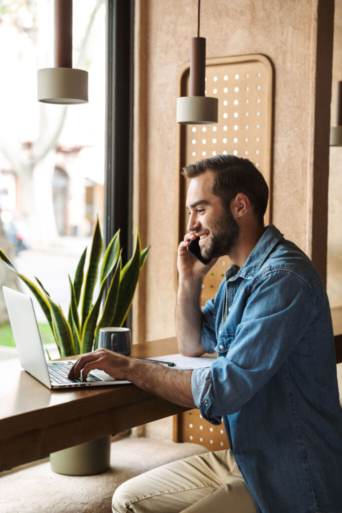 Homme dans un café travaillant sur son ordinateur tout en passant un appel sur son téléphone mobile