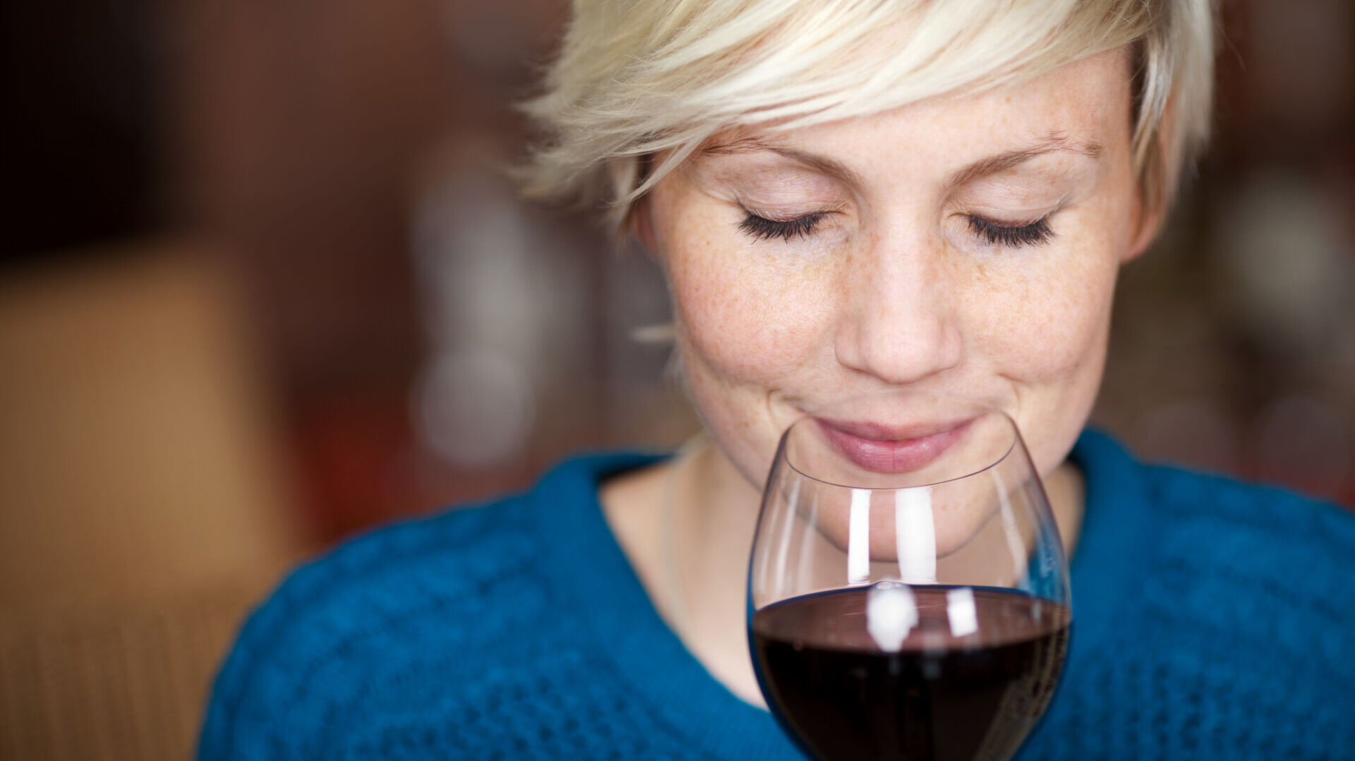 Femme blonde sentant un verre de vin rouge.