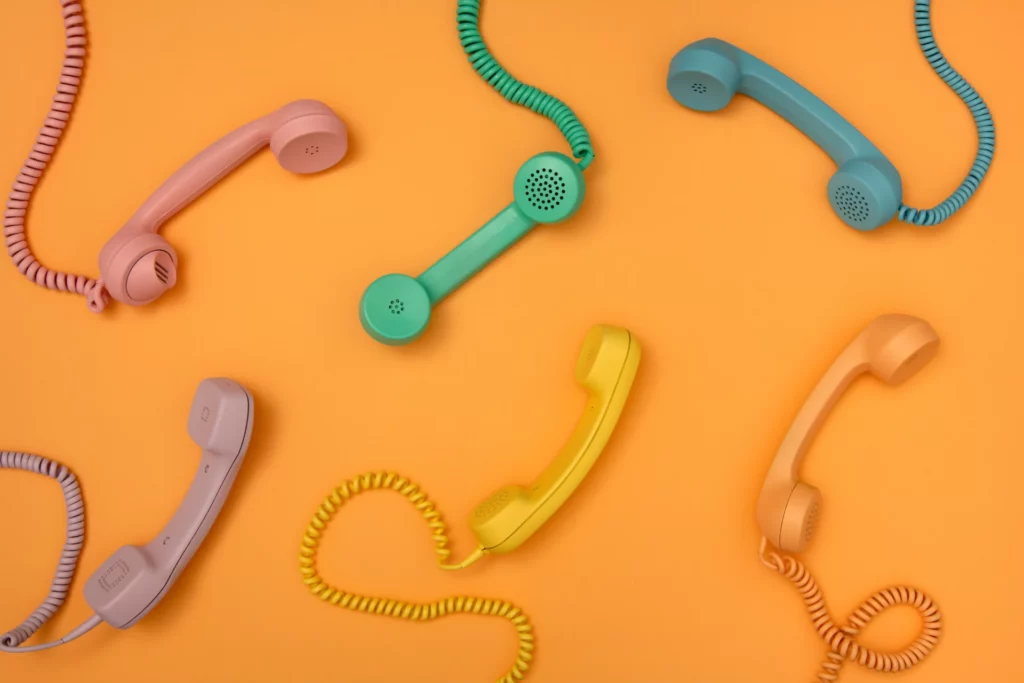 Différents combinés téléphoniques colorés sur fond orange pour représenter la diversité des solutions d'accueil téléphonique