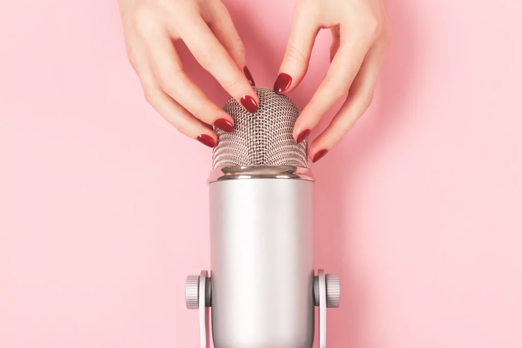 Gros plan sur des mains féminines avec du vernis à ongles rouge ajustant un microphone argenté sur fond rose