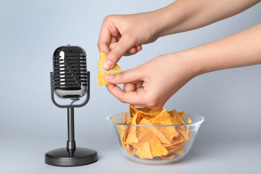 Mains croquant des chips près d'un microphone noir avec un bol de chips en arrière-plan