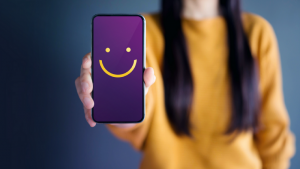 Personne tenant un smartphone avec un visage souriant à l'écran, symbolisant une expérience client positive.