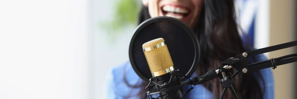 Personne souriante en train d'enregistrer un message avec un microphone doré