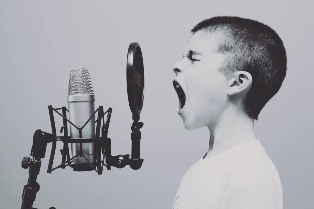 Photo en noir et blanc d'un enfant criant dans un microphone, symbolisant l'expression et la communication vocale dans un podcast.